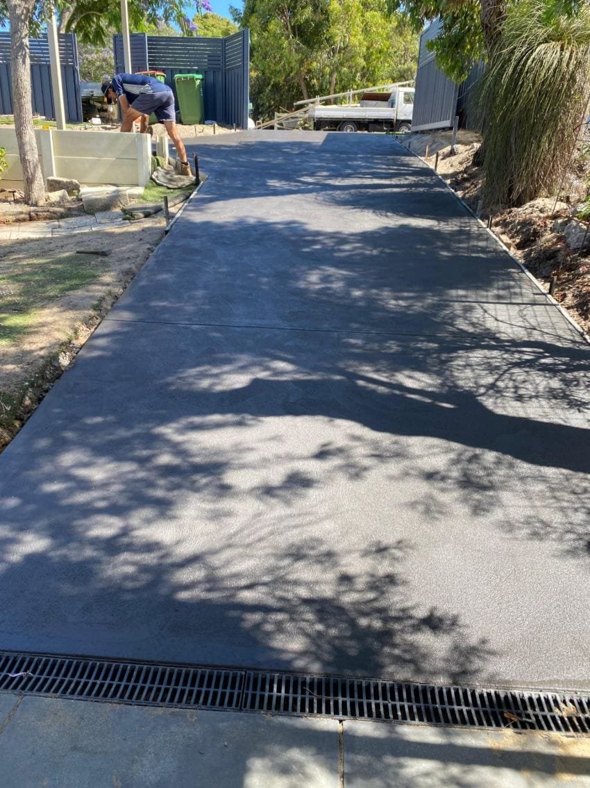 Charcoal-coloured concrete driveway finished on a leafy Perth block